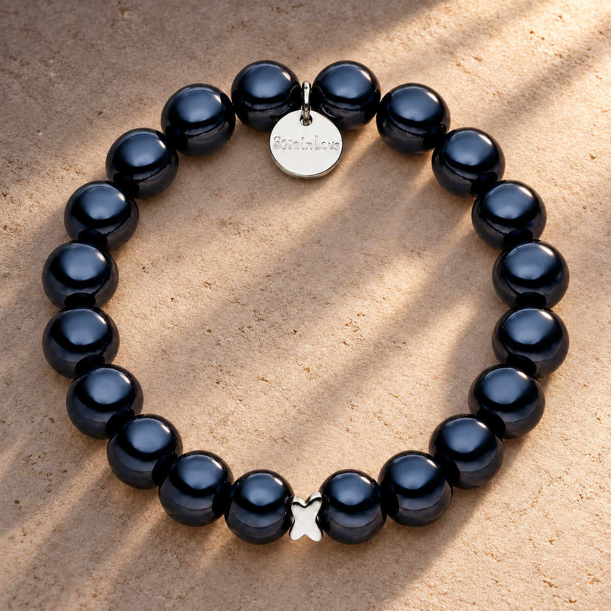 Schwarzes Perlenarmband mit silbernem Schmetterlingsdetail auf champagnerfarbenem Hintergrund im warmen Abendlicht