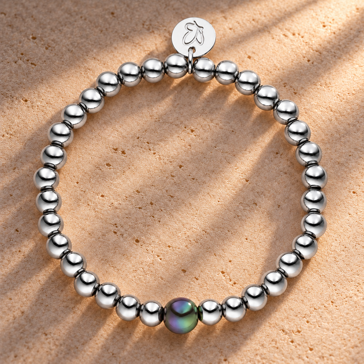 Perlenarmband Versilbert Fine Dunkelgrau mit 3D Intensiv Glow Effekt 6mm – auf champagnerfarbenem Hintergrund im warmen Abendlicht.