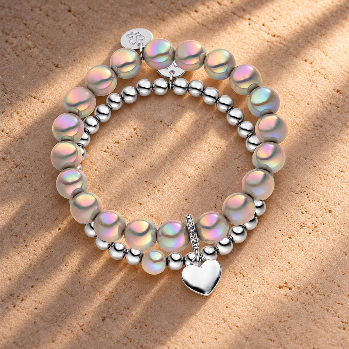 Perlenarmband Set mit Herzanhänger Hellgrau - 3D Intensiv Glow Effekt & Versilbert – auf champagnerfarbenem Hintergrund im warmen Abendlicht.