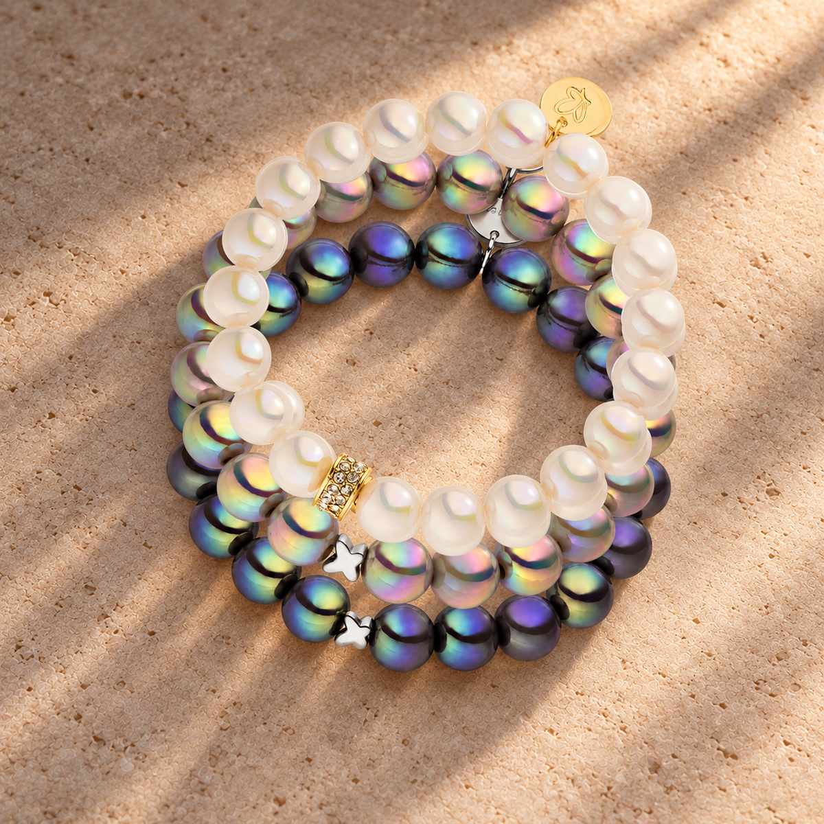 Perlenarmband-Set Weiß–Dunkelgrau–Hellgrau mit Schmetterlingen – 3D Intensiv Glow 10 mm – auf champagnerfarbenem Hintergrund im warmen Abendlicht.
