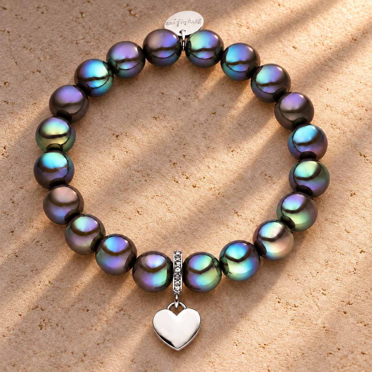Perlenarmband mit Herzanhänger Dunkelgrau mit 3D Intensiv Glow Effekt 10mm – auf champagnerfarbenem Hintergrund im warmen Abendlicht.