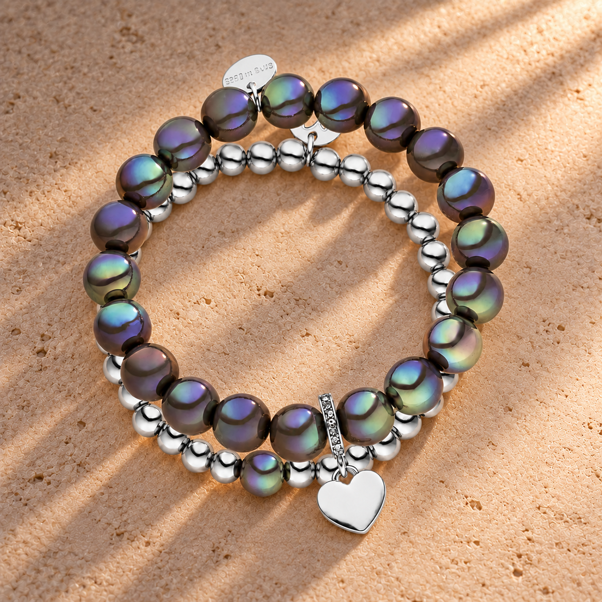 Perlenarmband Set mit Herzanhänger Dunkelgrau - 3D Intensiv Glow Effekt & Versilbert – auf champagnerfarbenem Hintergrund im warmen Abendlicht.