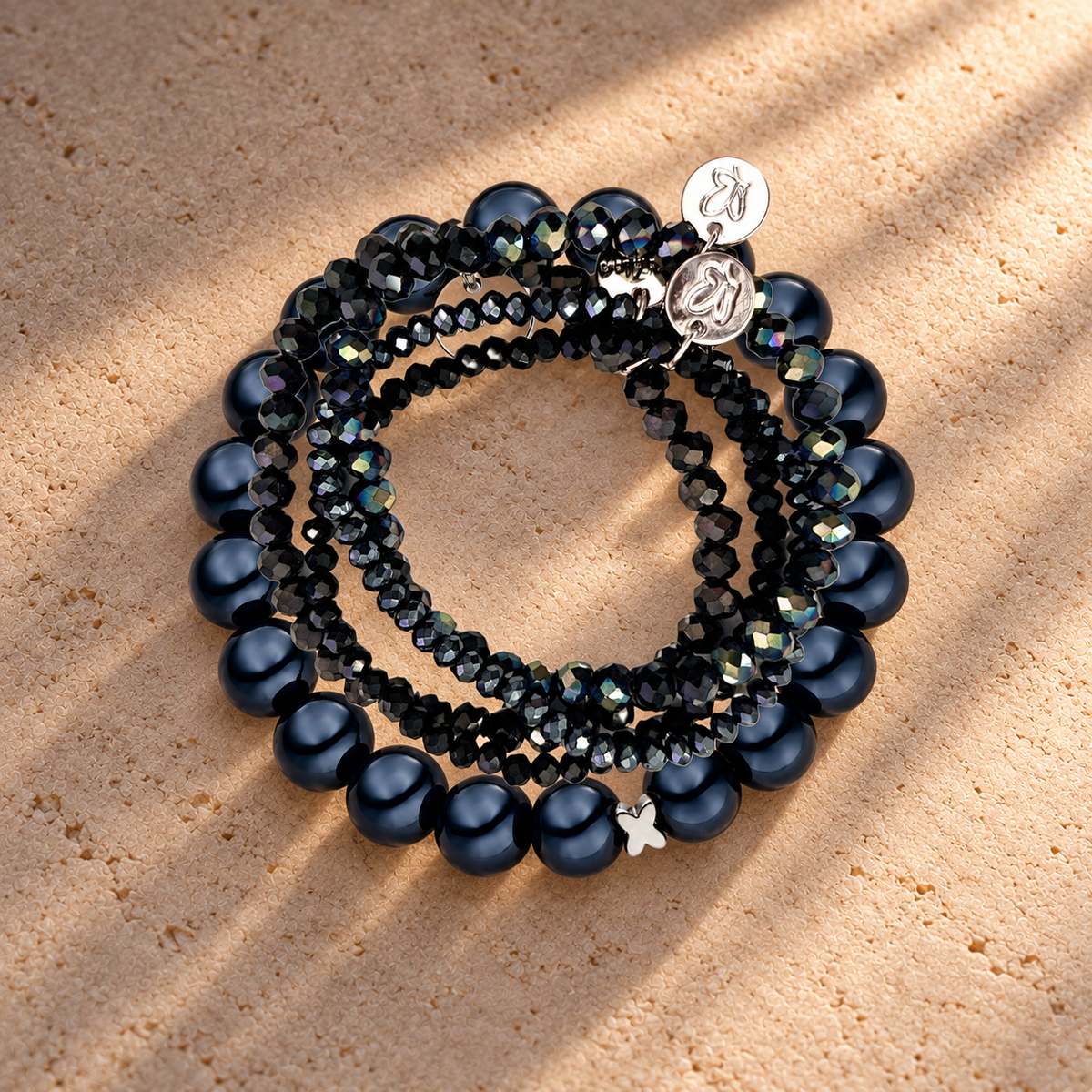 Perlenarmband-Set Schwarz mit Schmetterling – 5-teilig mit 3D Intensiv Glow 12 mm – auf champagnerfarbenem Hintergrund im warmen Abendlicht.